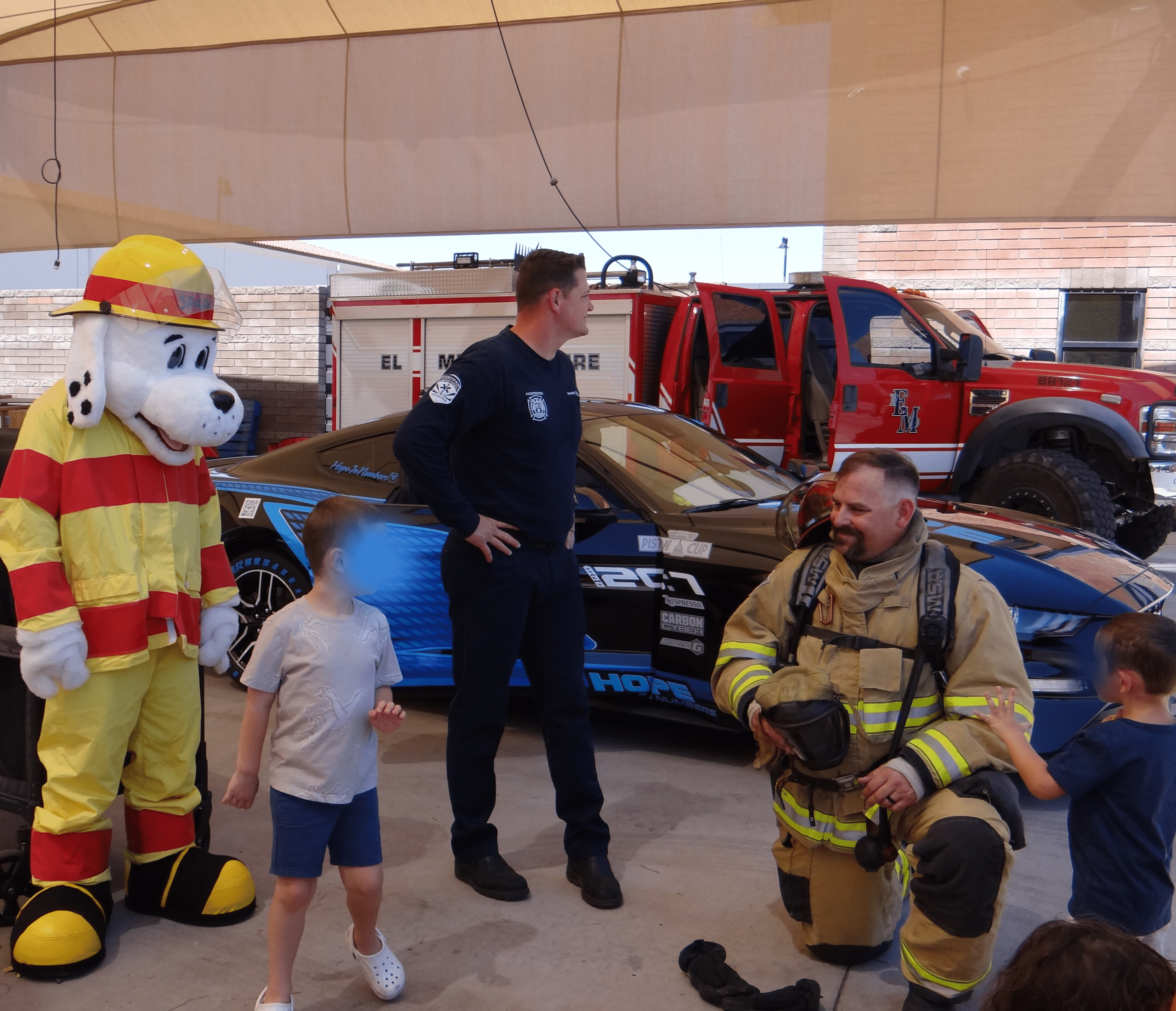 Fireme and children standing in front of Fire department automobiles.